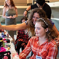 Camper admiring her make-up in a mirror with her make-up artist looking over her shoulder