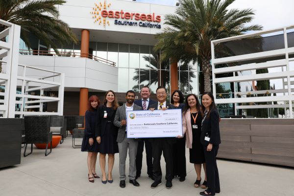 Eight people stand in front of the Easterseals Irvine building holding a check for $1 million.