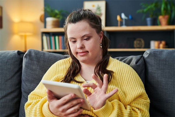 Woman in yellow sweater looking down at tablet she's working on.