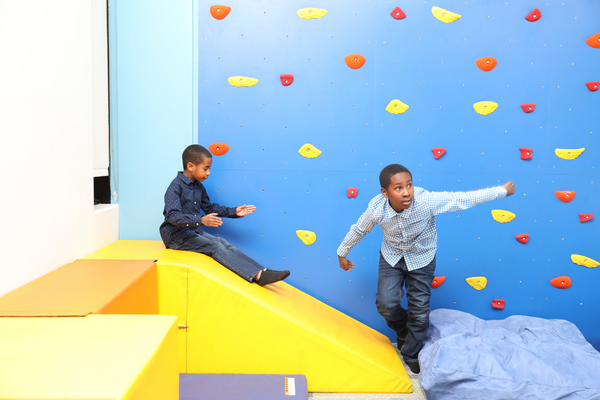 Evan and Ethan playing on the colorful rock wall in the gym.