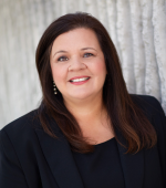 A woman with brunette hair wearing a black blouse and blazer smiling for her headshot.