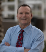 A white man with brown hair and wearing a blue collared button down and colorful red tie