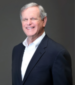 A white man with grey hair wearing a navy blazer and white collared button down smiling for his headshot. 