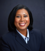 A black woman with black hair wearing a navy blazer and blue button up smiling for her headshot