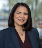 A woman with black hair wearing a black blazer and burgundy shirt smiling for her headshot