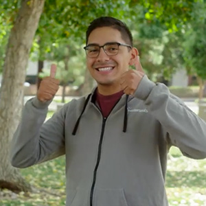 Hispanic man in grey zip up hoodie giving thumbs up while smiling