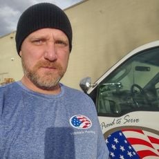 Photo shows man with beard wearing a black beanie and blue shirt taking a selfie