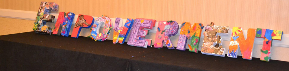 The word empowerment on a table, where each letter is a wooden block decorated with art by Thrive participants. . 