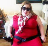 Woman in red dress, wearing sunglasses, smiling and sitting in her wheelchair indoors