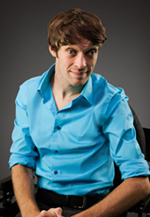 picture of Zach sitting in a chair, smiling, wearing a blue dress shirt 