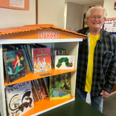 Ray Bell proudly standing beside the community library he crafted with love and dedication.