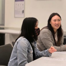 Josephine wearing a face mask and speaking with someone seated at a desk