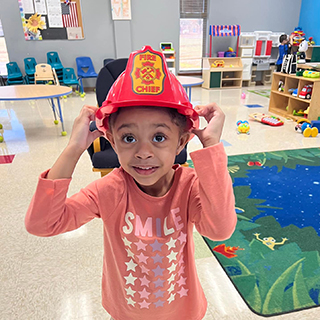 Little girl in pink shirt wearing a firefighter hat
