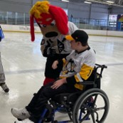 Guy in wheelchair on ice rink with hockey mascot