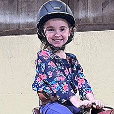 girl with helmet smiling at camera from atop a horse (horse not in image)